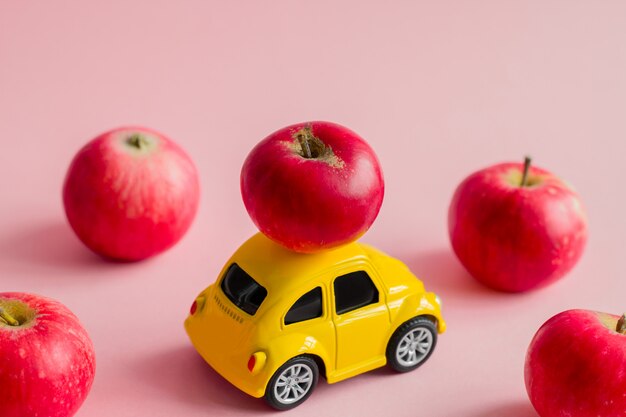 Pequeno Coche De Adorno Amarillo Con Manzanas Rojas En Un Rosa Pastel Foto Premium