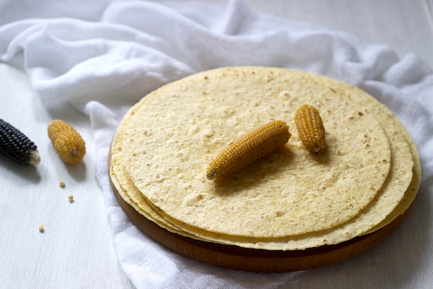 Una pila de tortillas de maíz redondas sobre tabla de madera y mazorcas de maíz. Foto Premium 