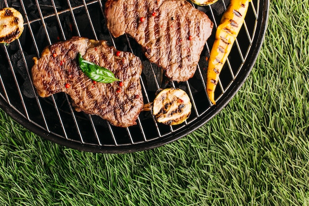 Preparación de bistec a la parrilla y verduras en la parrilla de barbacoa sobre estera de hierba Foto gratis