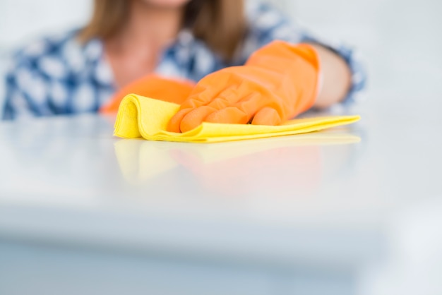El primer de los guantes que llevan de la mujer limpia el escritorio blanco con la servilleta amarilla Foto gratis
