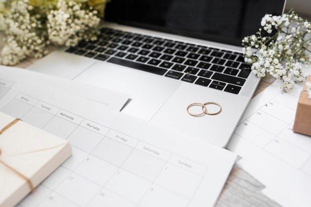 Primer Plano Del Calendario Anillos De Boda Aliento De Bebe Flores Y Computadora Portatil En El Escritorio Foto Gratis