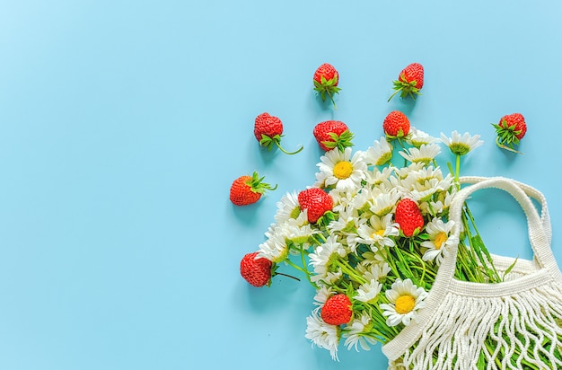 Ramo de margaritas de campo en bolsa de malla ecológica comercial reutilizable y fresas rojas sobre fondo azul. Foto Premium