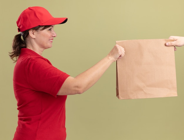 Repartidor De Mediana Edad En Uniforme Rojo Y Gorra Dando Paquete De Papel A Un Cliente 0970