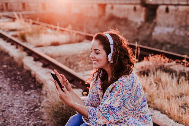 Retrato al aire libre de una joven bella mujer al atardecer escuchando música en auriculares y sonriendo Foto Premium