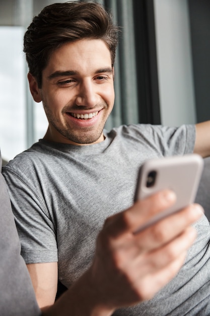 Retrato De Un Atractivo Joven Barbudo Sonriente Vistiendo Ropa Casual Sentado En Un Sofá En La 