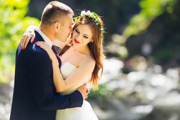 Retrato De Boda De Hermosos Recién Casados La Novia Sonríe Abraza Al Novio Que Besa La Mejilla 