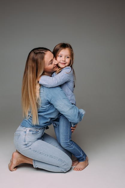 Retrato de estudio de feliz madre adulta en mezclilla abrazando a su pequeña hija también