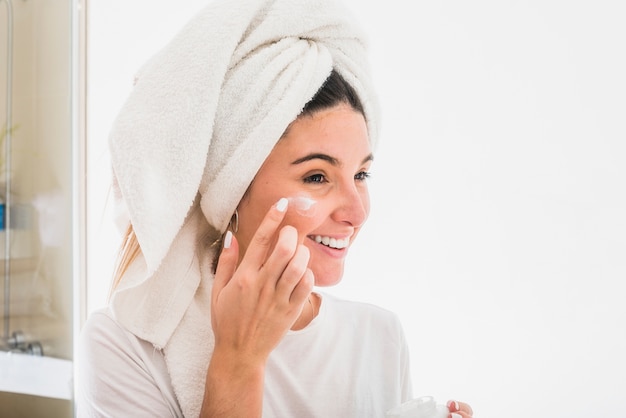 Retrato feliz de una mujer joven que aplica la crema en su cara ...