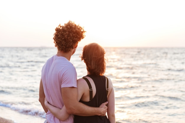 Retrato De Una Hermosa Joven Pareja Abrazándose En La Playa Mirando Al Amanecer Foto Premium 