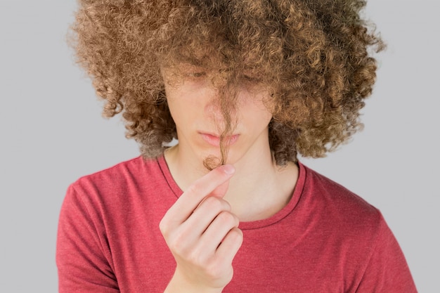 Retrato De Un Hombre Europeo Rizado Joven Que Mira Preocupado Su Pelo Largo Sostiene Un Rizo De Pelo Con Sus Dedos Muy Chico Exuberante Pelo Chico Cabello Rizado Para Hombres Foto