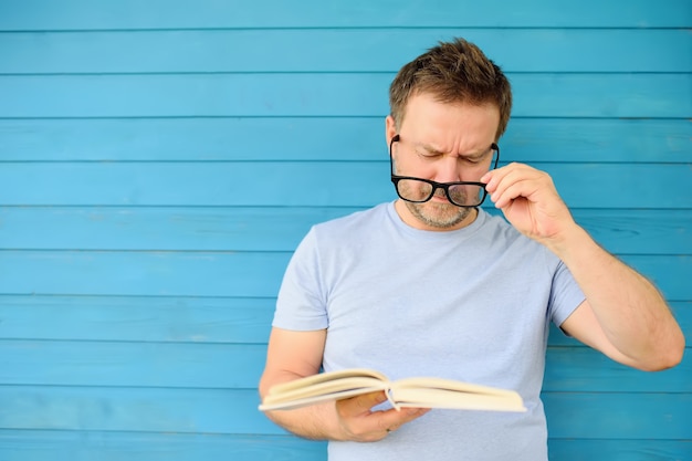 Retrato de un hombre maduro con anteojos negros grandes que intenta leer el libro pero que tiene dificultades para ver el texto Foto Premium