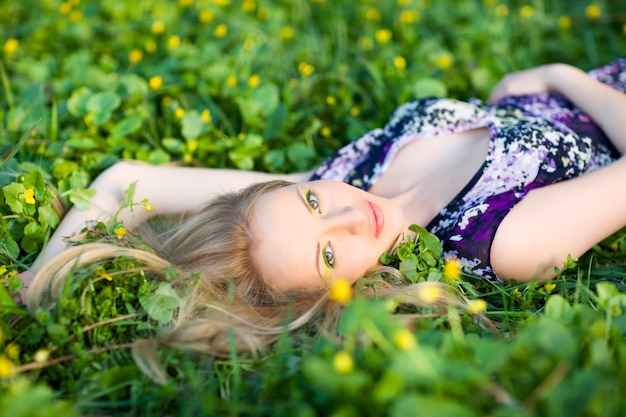 Retrato de joven hermosa mujer rubia tumbada en la hierba y flores en día de verano Foto Premium