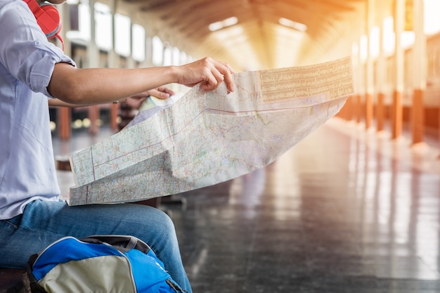 Retrato lateral de un joven viajero sentado con mapa de elegir dÃ³nde viajar y la bolsa de espera para el tren, filtro de tono vintage efectuado