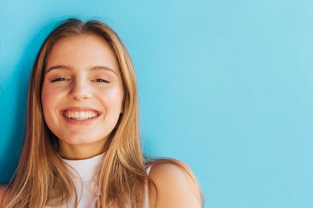 Retrato de una mujer joven alegre que mira la cámara contra el contexto azul Foto gratis