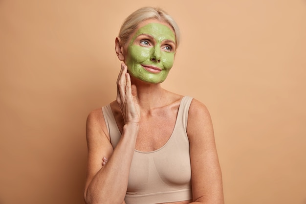 Retrato de mujer de mediana edad soñadora aplica máscara verde en la