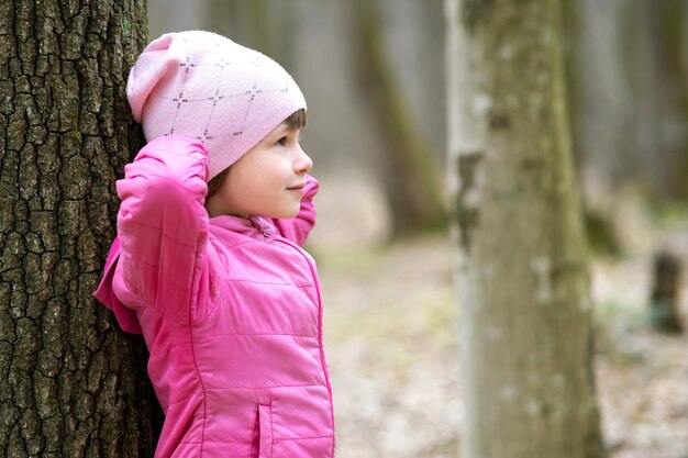 Retrato De Niña Bonita Joven Vistiendo Chaqueta Rosa Y Gorra Inclinada A Un árbol En El Bosque 7028