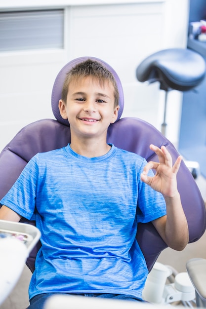 Retrato de un niño feliz que se sienta en la silla dental que gesticula