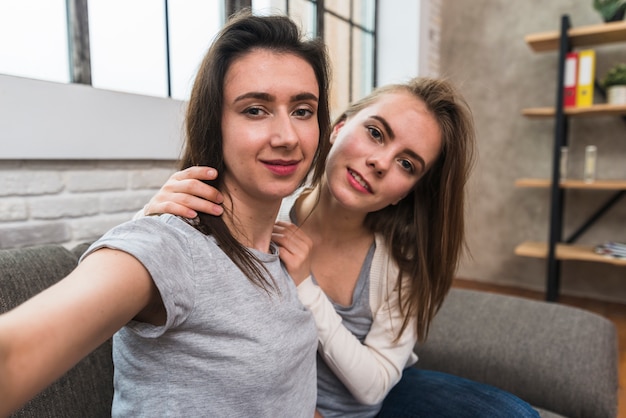 Retrato de una pareja joven lesbiana sonriente sentada en el sofá tomando selfie Foto gratis