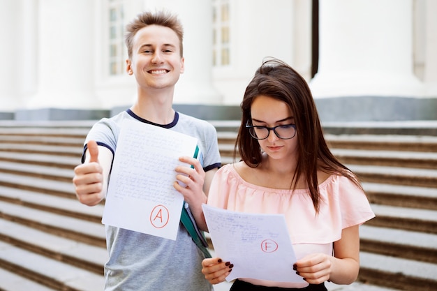 Retrato De Vista Frontal De Dos Estudiantes Mostrando Examenes