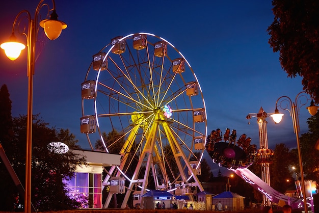 Rueda de la fortuna iluminada en el parque de atracciones en la ciudad