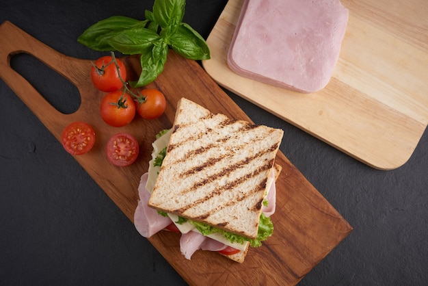 Sándwich a la plancha con jamón, queso, tomate y lechuga servido sobre tabla de cortar de madera. Foto gratis
