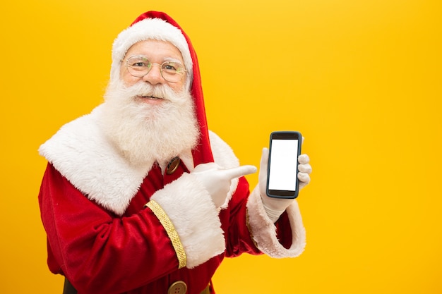 Santa claus con celular sobre fondo amarillo Foto Premium