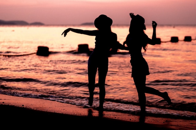Silueta de dos mujeres jóvenes divirtiéndose en la playa del mar Foto Premium