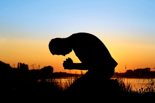 Silueta de hombre al atardecer orando a dios | Foto Premium