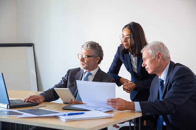Socios concentrados que usan laptop y trabajan con documentos. empresarios serios confiados en trajes de oficina discutiendo juntos el proyecto de la empresa. concepto de gestión, negocios y asociación Foto gratis