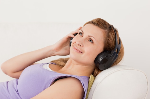 Sonriente rubia mujer escuchando música tumbada en el sofá Foto Premium