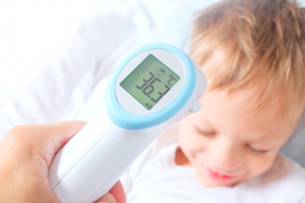 Un termómetro infrarrojo digital sin contacto registró la temperatura corporal normal de un niño. el niño se está recuperando de una enfermedad. prevención exitosa de resfriados y gripe en niños. Foto Premium