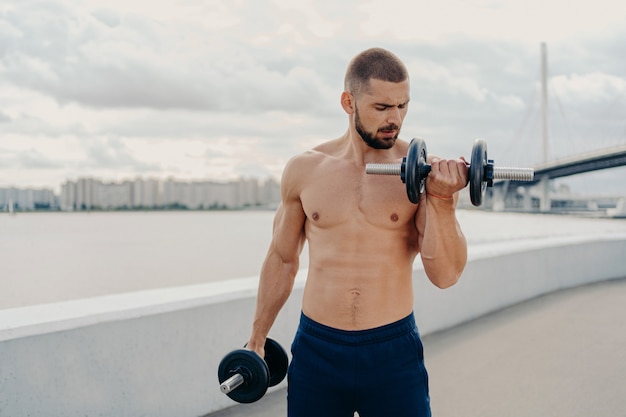 Un Tipo Musculoso Con Torso Desnudo Se Ejercita Con Pesas Se Para Sin Camisa Entrena Los