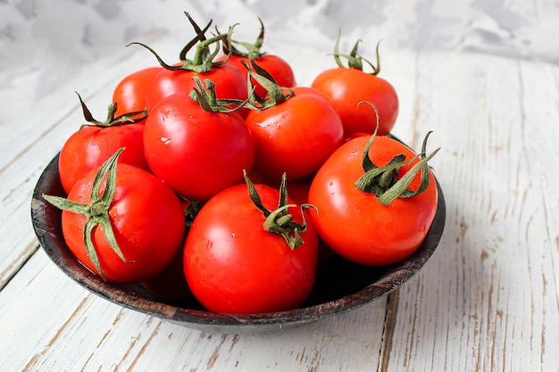 Tomates rojos orgánicos frescos en placa negra en la mesa de madera blanca con pimientos verdes y rojos y pimientos, pimientos verdes, granos de pimienta negra, sal, primer plano, concepto saludable Foto gratis