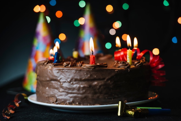 Torta de cumpleaños con una vela iluminada contra luz de fondo y sombrero  de fiesta | Foto Premium