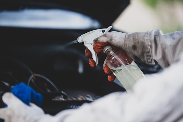 Trabajador de lavado de autos con un uniforme blanco de pie con una esponja para limpiar el automóvil en el centro de lavado de automóviles, concepto para la industria del cuidado del automóvil. Foto gratis