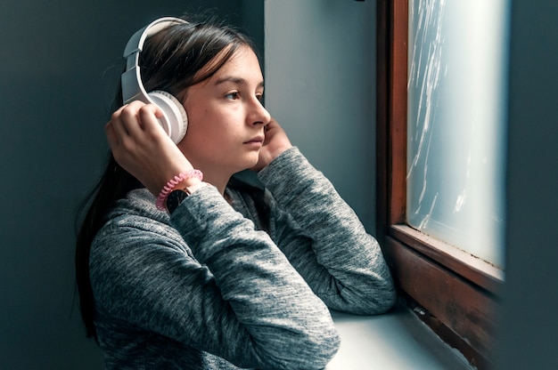 Triste adolescente sentado en el alféizar de la ventana con auriculares escuchando música | Foto ...
