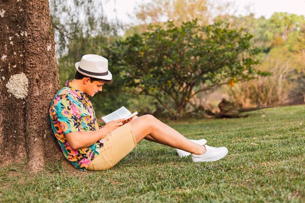 Turista con sombrero y camisa de flores, lee un libro en el Turista con sombrero y camisa de flores, lee un libro en el