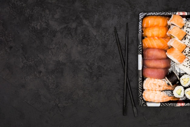 La variedad de pescados asiáticos rueda en la bandeja y los palillos sobre fondo texturizado con el espacio para el texto Foto gratis