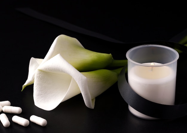 Una Vela Con Una Cinta Negra De Luto Junto A Una Flor Blanca Y Pastillas Foto Premium