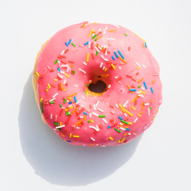 Una vista elevada de rosquillas rosadas con chispas sobre fondo blanco Foto gratis