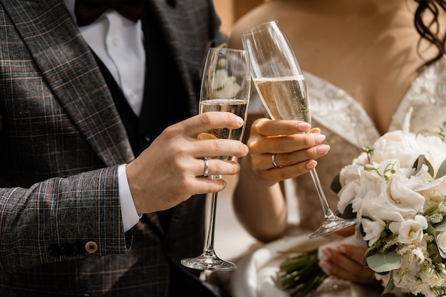 Vista frontal de las manos de los novios con copas de champán y bouquet de bodas Foto gratis