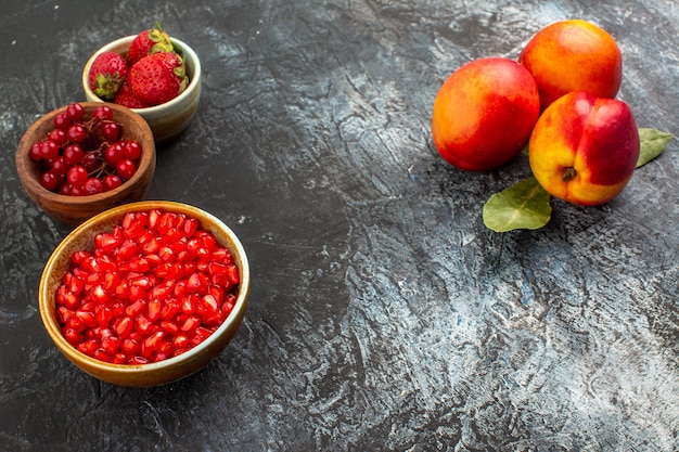 Vista frontal de melocotones frescos con frutos rojos en el jardín de árboles frutales de mesa claro-oscuro Foto gratis