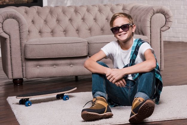 Vista frontal del niño con gafas de sol sentado en el piso Foto Gratis