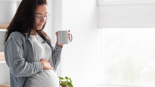 Vista lateral de la mujer embarazada en casa con taza de café Foto gratis