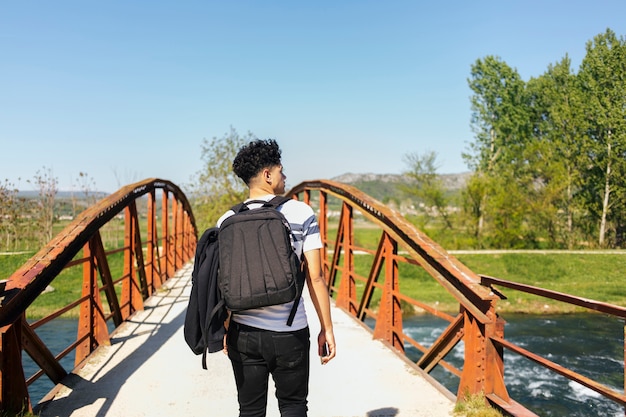 Vista trasera del hombre joven que camina en el puente sobre el río