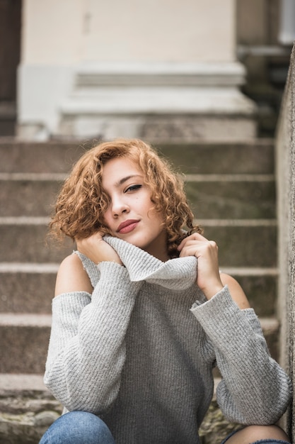 Affascinante signora sorridente che tiene il colletto del maglione e seduto sui gradini Foto Gratuite