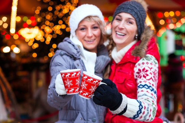 Amici che bevono vino aromatizzato sul mercatino di natale Foto Premium