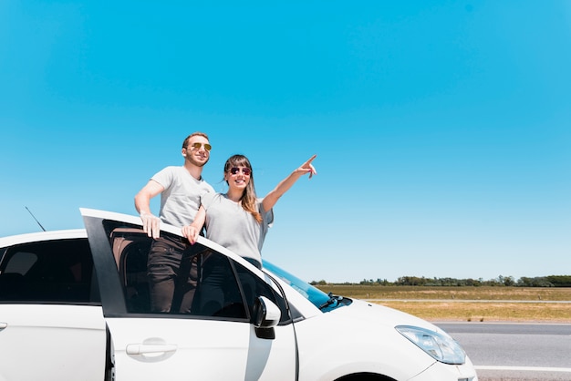 Amici sorridenti che si siedono su un'auto che indica a qualcosa Foto Gratuite
