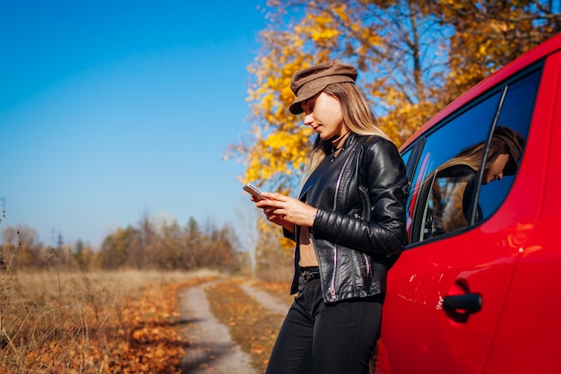 Automobile facente una pausa della giovane donna che per mezzo dello smartphone sulla strada di autunno. il conducente ha interrotto l'auto per catturare un segnale migliore Foto Premium