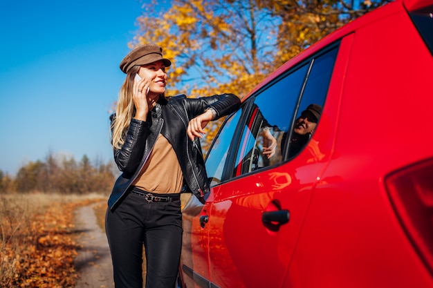 Automobile facente una pausa della giovane donna che per mezzo dello smartphone sulla strada di autunno. il driver si è fermato automaticamente nella foresta per chiamare Foto Premium